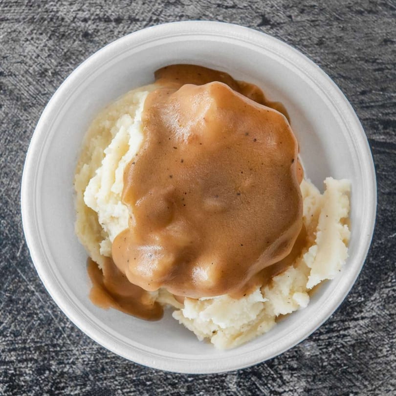 Creamy mashed potatoes topped with rich brown gravy, served in a white bowl.