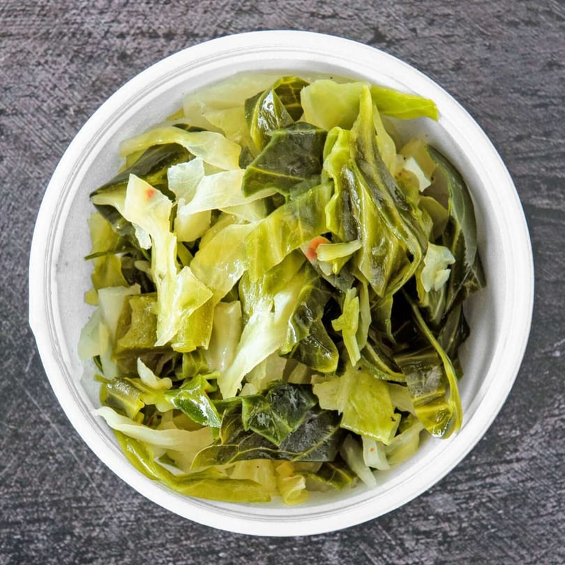A white bowl filled with a mix of cooked collard greens and cabbage, seen from above.
