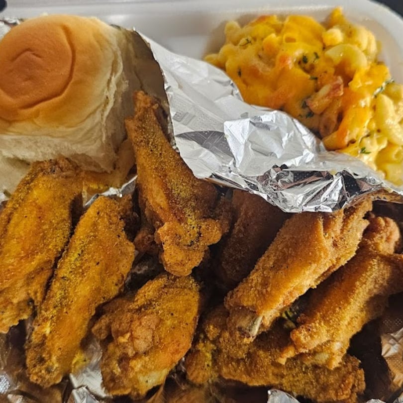 Southern fried chicken wings, macaroni and cheese, and a dinner roll in a takeout container.